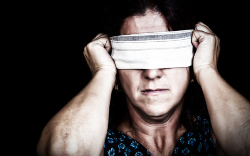 Grunge image of a serious woman with a handkerchief covering her eyes to avoid seeing isolated on black