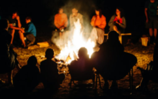 Blurred People sit at night round a bright bonfire