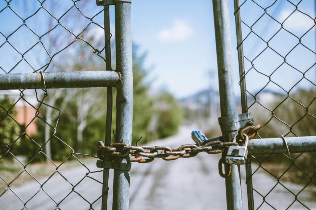 Two wire gates padlocked shut with a view down a road.